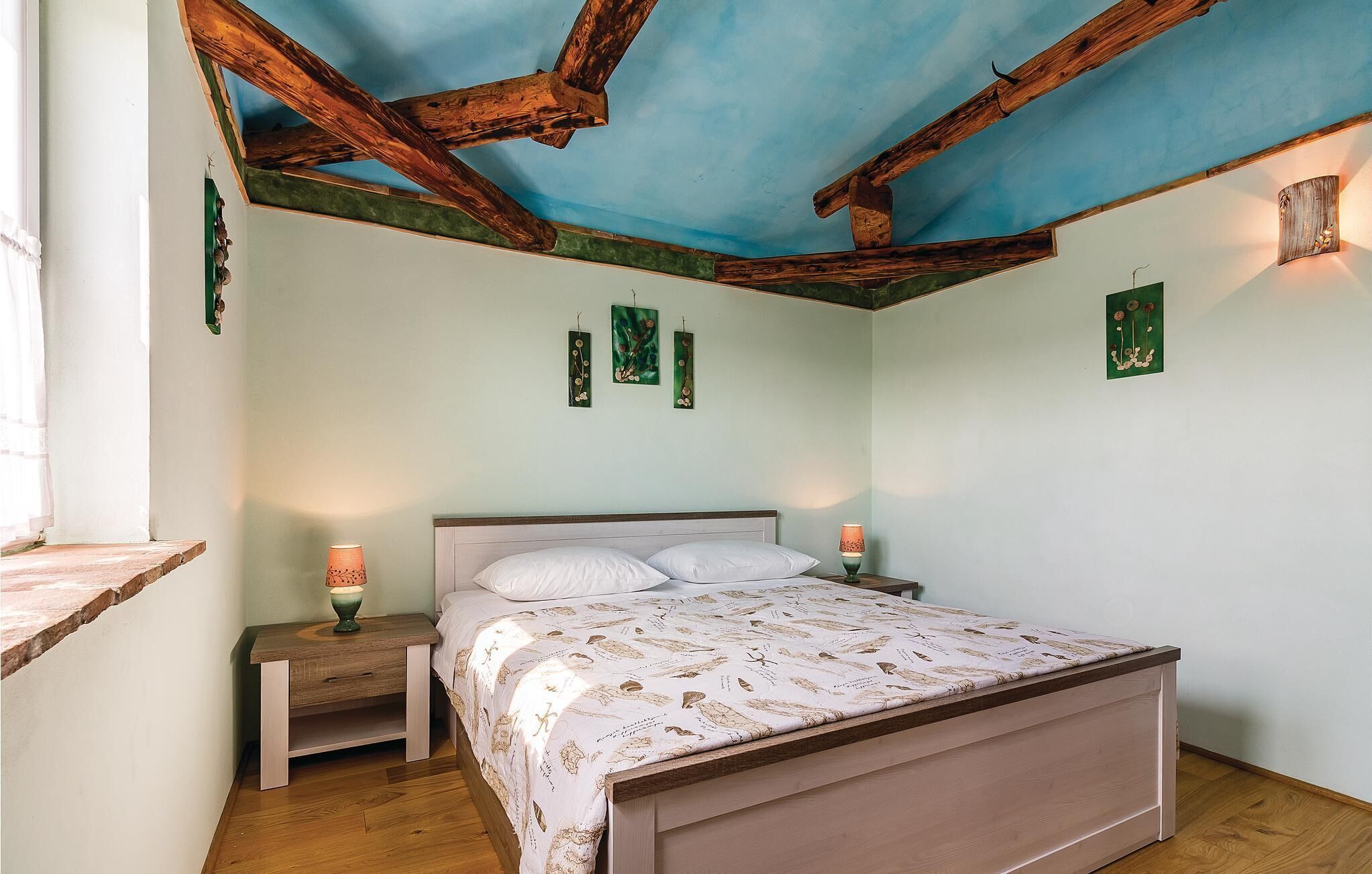 Ein Schlafzimmer mit Holzboden, einem Bett mit gemustertem Überwurf, zwei Nachttischlampen und Wandbildern.