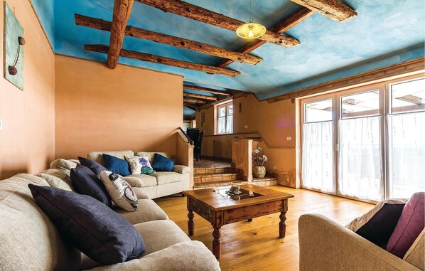 Un salón acogedor con techo de madera, un conjunto de sofás, una mesa de centro y una escalera que lleva a un nivel superior.