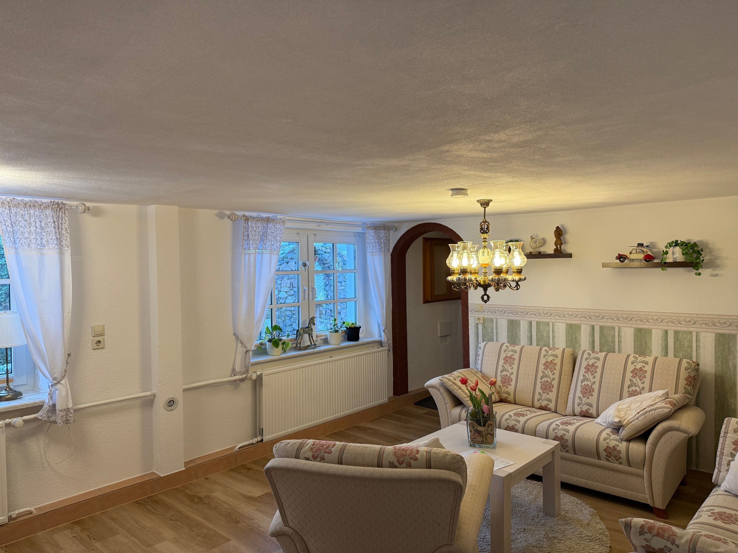 A cozy living room with a sofa set, a chandelier, and a window with curtains.
