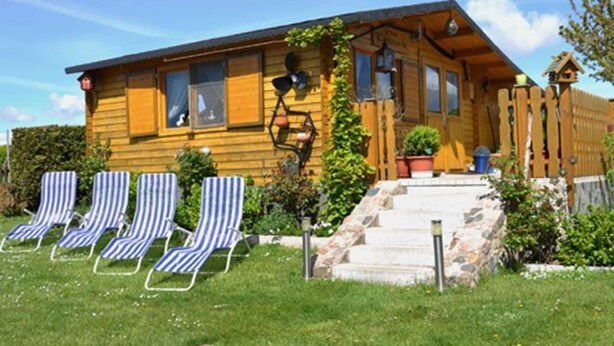 Une cabane en bois avec un porche, quatre chaises longues à rayures et un escalier en pierre menant à l’entrée.