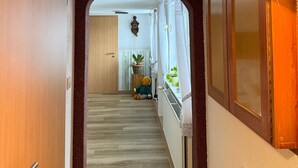 Un couloir avec une porte en bois sur la gauche, une arche à cadre en bois et une fenêtre ornée d’une plante sur la droite.