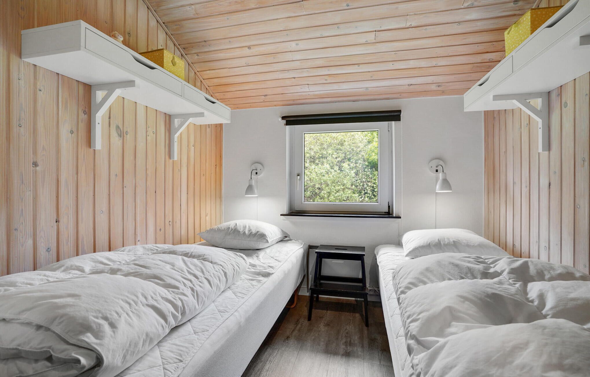 Ein Zimmer mit zwei Einzelbetten, Holzwänden, einem Fenster mit Blick auf Grünflächen und Wandlampen.