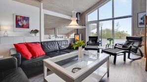 A modern living room with a black leather sofa, a glass coffee table, and a large window offering a view of the outdoors. - Awesome home in Ebeltoft with sauna (Ebeltoft)