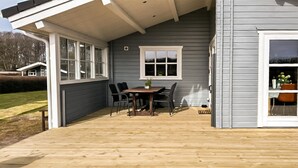 Un patio techado con cubierta de madera, una mesa con sillas y un ventanal.