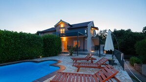 Una moderna casa con piscina, sedie a sdraio e un patio coperto.