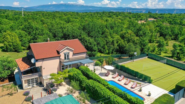 Una casa con campo da tennis, piscina e vista su una zona boschiva.