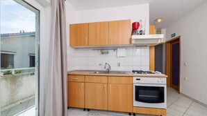 Une cuisine compacte avec des meubles en bois, un four encastré et une fenêtre donnant sur des immeubles.