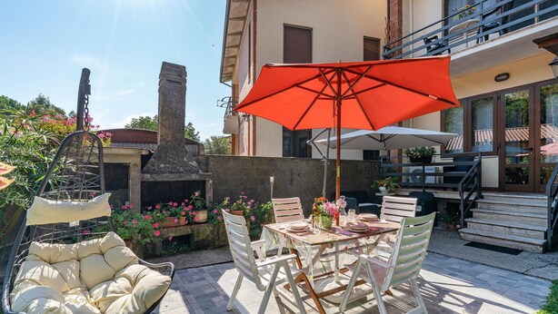 Un patio al aire libre con una mesa lista para comer, rodeado de sillas y una sombrilla.