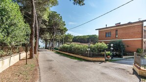 Una calle residencial tranquila con camino de grava, un edificio de ladrillo y una cerca con follaje.