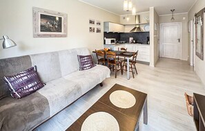 A living room with a sofa, coffee table, and dining area with chairs. There is a kitchen in the background with cabinets and a stove. - Gorgeous apartment in Darlowo with WiFi (Darlowo)