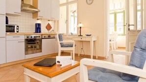 Eine kompakte Küche mit weißen Schränken, einer Mikrowelle, einem Backofen und einer Kaffeemaschine. Es gibt einen Essbereich mit Tisch, Stühlen und einer Lampe.