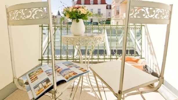 Ein Balkon mit Metallstuhl und Tisch, einer Blumenvase und einer Zeitschrift.