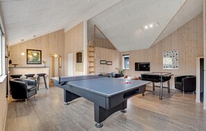 Relax in this spacious room with a high ceiling, featuring a pool table, foosball table, and comfortable seating.