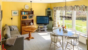 Ein Wohnzimmer mit einer Couch, Fernseher, Holzschrank und einem Esstisch mit Stühlen.