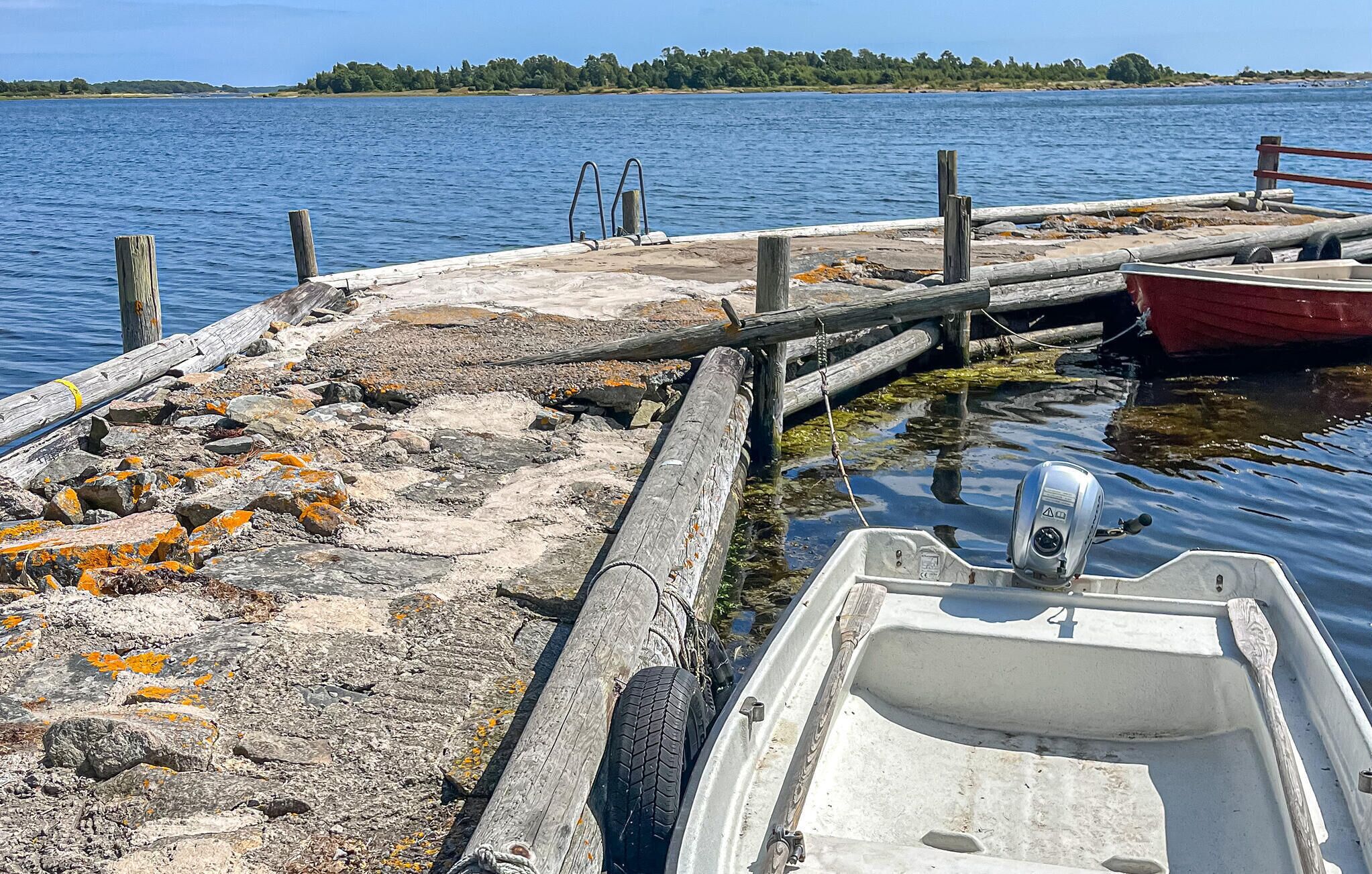 A boat docked at a rocky pier with a view of a calm lake and distant trees.