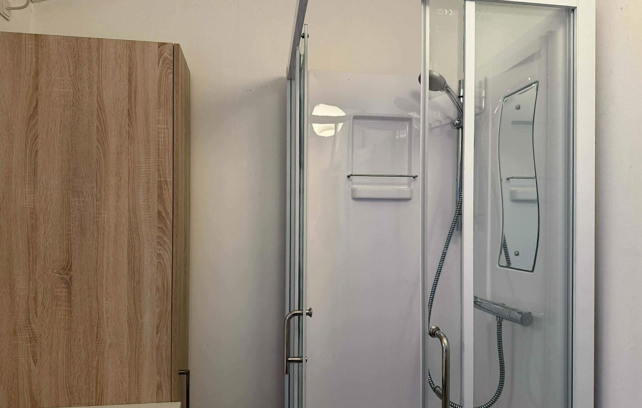 A glass-enclosed shower stall with a handheld showerhead and a handheld shower attachment.