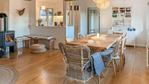 A cozy living room with a fireplace, wooden dining table, wicker chairs, and a bookshelf.