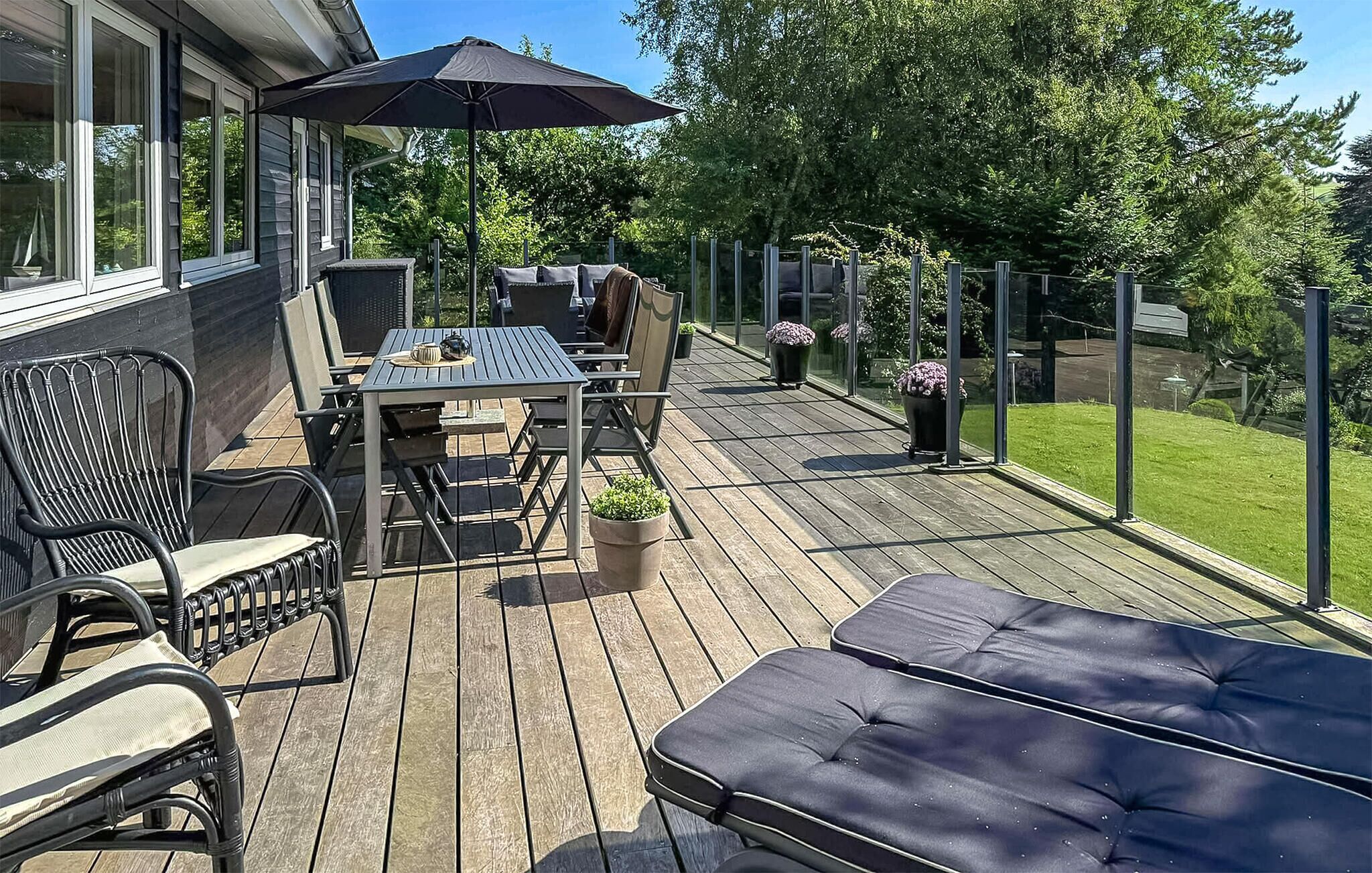 Una terraza de madera con una mesa y sillas, un banco acolchado y plantas en macetas.
