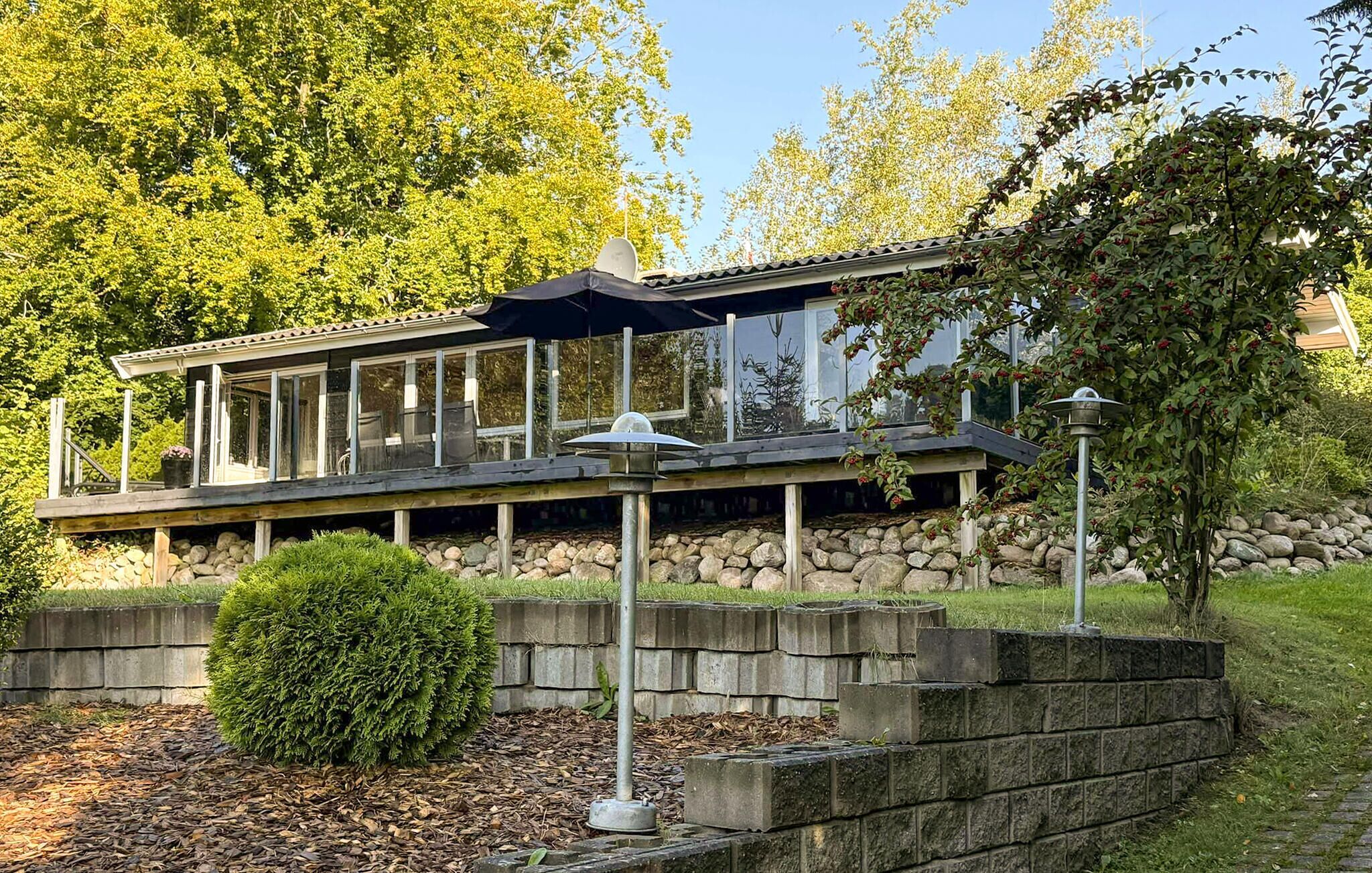 A modern house with a covered patio, stone retaining wall, and a well-maintained garden.