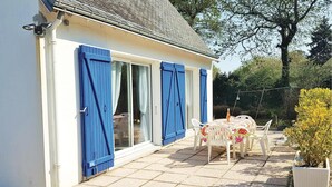 Een huis met een patio, een tafel en stoelen, een kleine tuin en een blauwe deur.