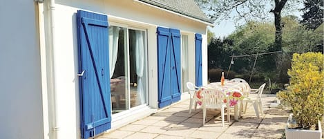 A house with a patio area featuring a table and chairs, a small garden, and a blue door.