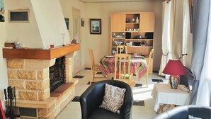 Een woonkamer met een open haard, een eettafel met stoelen, een boekenkast en een lamp.