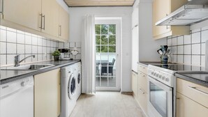 Et moderne køkken med indbygget vaskemaskine og tørretumbler, en komfur og et vindue med udsigt til det fri.