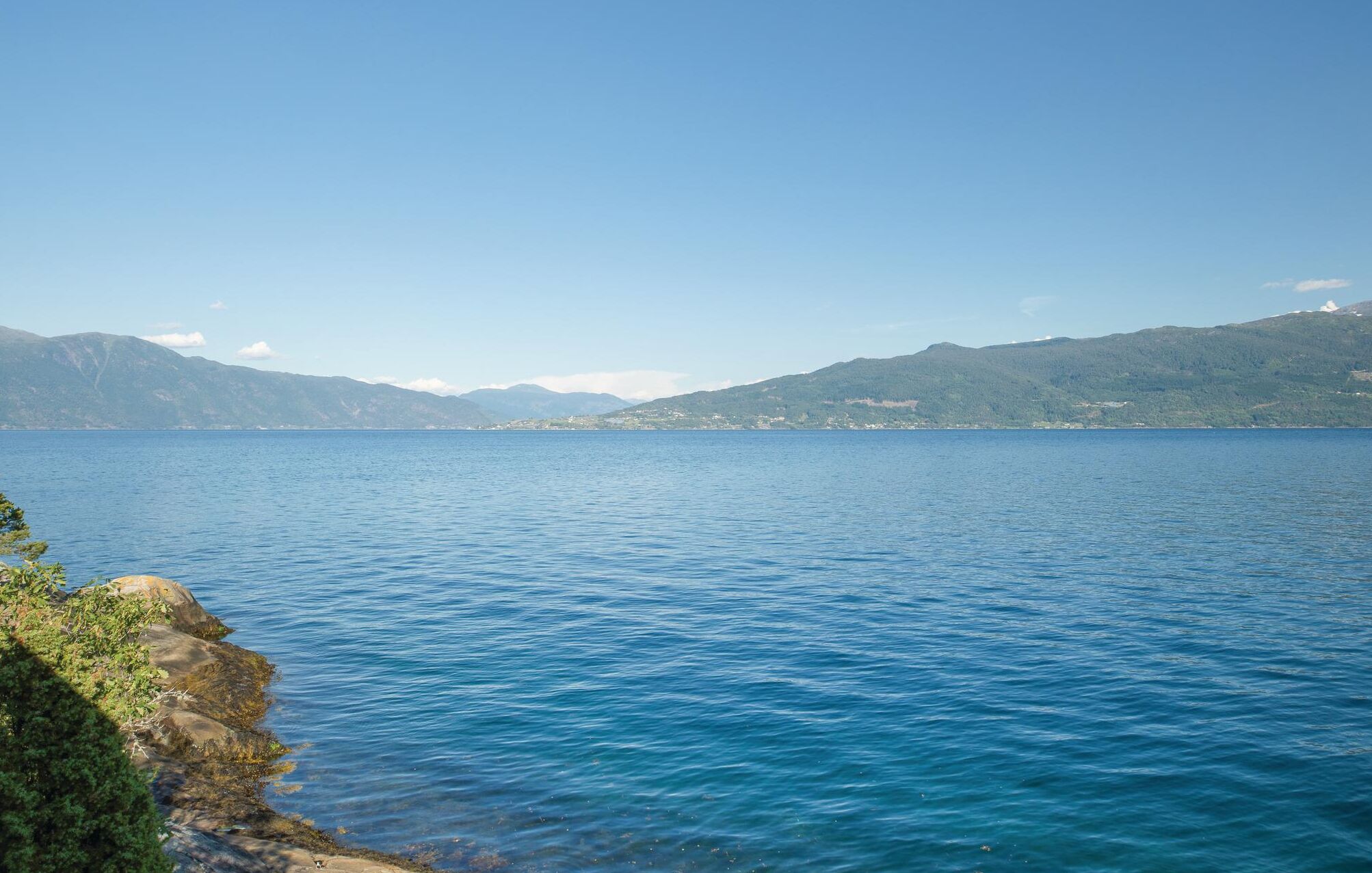 A calm lake with a rocky shoreline and distant mountains.