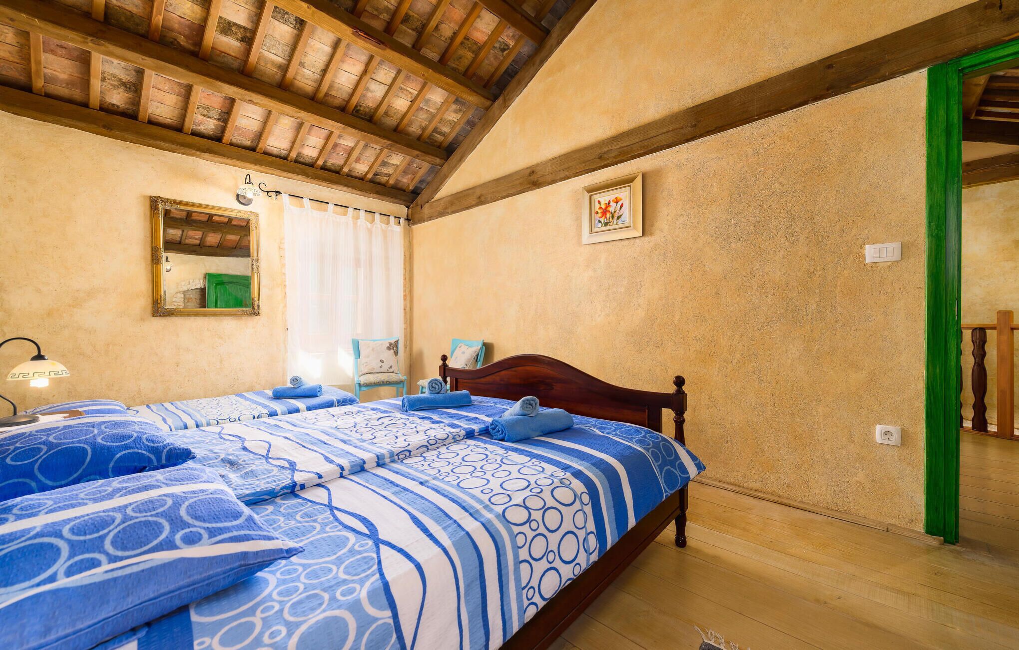 Ein Schlafzimmer mit Holzboden, einem Bett mit blau gemusterten Bettbezügen, einem Sessel, einem Nachttisch und einem Spiegel.
