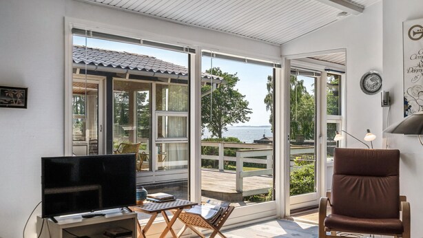 Een woonkamer met een televisie, een bruine leren fauteuil en uitzicht op zee door grote glazen deuren.