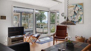 Een woonkamer met een televisie, een bruine leren fauteuil, een glazen deur die uitkomt op een terras, en een schilderij aan de muur.
