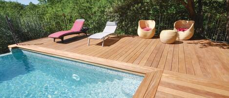 Una terraza de madera con piscina, dos sillas reclinables y dos sillones de mimbre.
