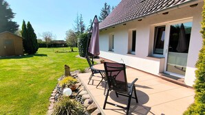 A patio with a table and chairs, a covered area, and a view of a house with a tiled roof and windows. - Rügen-Fewo 123 - apartment (Patzig on Rügen)