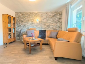 A living room with a stone wall, a wooden cabinet, a leather sofa, and a small table with a vase. - Rügen-Fewo 123 - apartment (Patzig on Rügen)