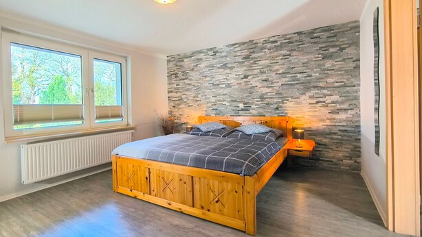 A bedroom with a wooden bed, a stone wall, a window with blinds, and a radiator. - Rügen-Fewo 123 - apartment (Patzig on Rügen)