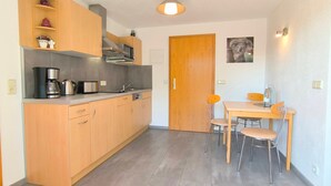 A compact kitchen with wooden cabinets, a built-in microwave, and a coffee maker. There is a dining area with a wooden table and chairs. - Rügen-Fewo 123 - apartment (Patzig on Rügen)