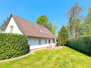 A single-story house with a tiled roof, a small porch with a table and chairs, and a well-maintained lawn. - Rügen-Fewo 123 - apartment (Patzig on Rügen)