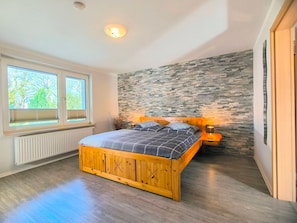 A bedroom with a wooden bed, a stone wall, a window with blinds, and a radiator. - Rügen-Fewo 123 - apartment (Patzig on Rügen)