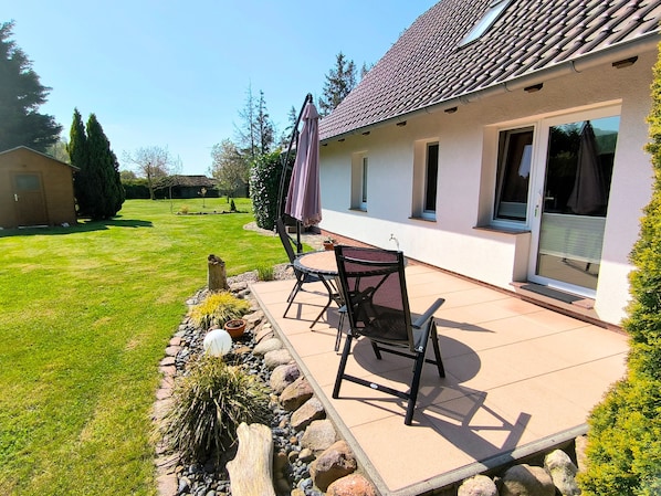A patio with a table and chairs, a covered area, and a view of a house with a tiled roof and windows. - Rügen-Fewo 123 - apartment (Patzig on Rügen)