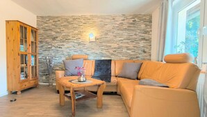 A living room with a stone wall, a wooden cabinet, a leather sofa, and a small table with a vase. - Rügen-Fewo 123 - apartment (Patzig on Rügen)