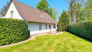 A single-story house with a tiled roof, a small porch with a table and chairs, and a well-maintained lawn. - Rügen-Fewo 123 - apartment (Patzig on Rügen)