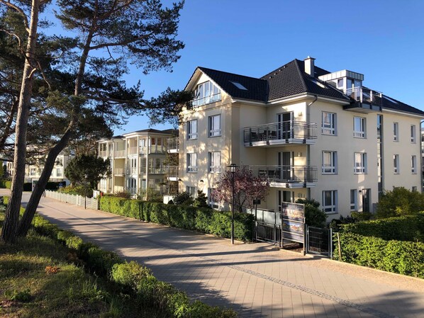 A multi-story residential building with balconies, a paved driveway, and surrounding greenery.