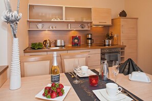 A modern kitchen with wooden cabinets, a coffee machine, and a dining area set with a bottle of wine, strawberries, and a red candle.