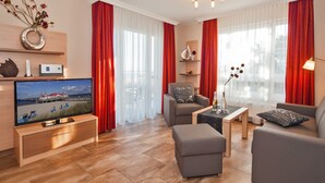 Un saló modern amb un televisor de pantalla plana, sofàs grisos, una taula de centre i cortines vermelles.