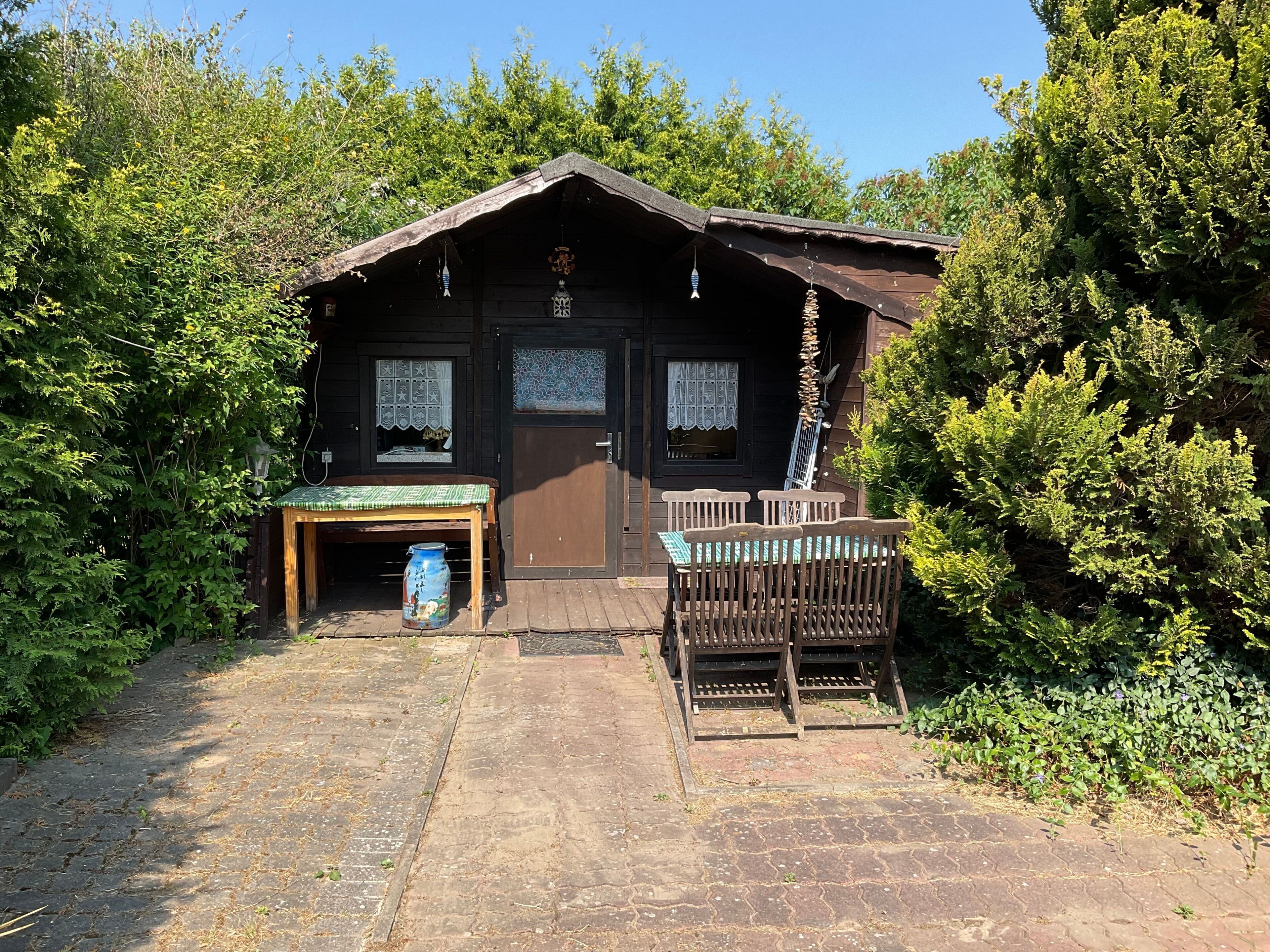 Une cabane rustique en bois, avec un toit de chaume, un banc en bois et une table recouverte d’une nappe verte.