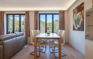 A dining area with a table and chairs, large windows with curtains, a sofa, and a painting on the wall. - Gorgeous apartment in Binz with indoor swimming pool (Prora/Rügen)