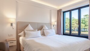 A hotel room with a large bed, two bedside lamps, a nightstand, a chair, and a window with a view of trees. - Gorgeous apartment in Binz with indoor swimming pool (Prora/Rügen)