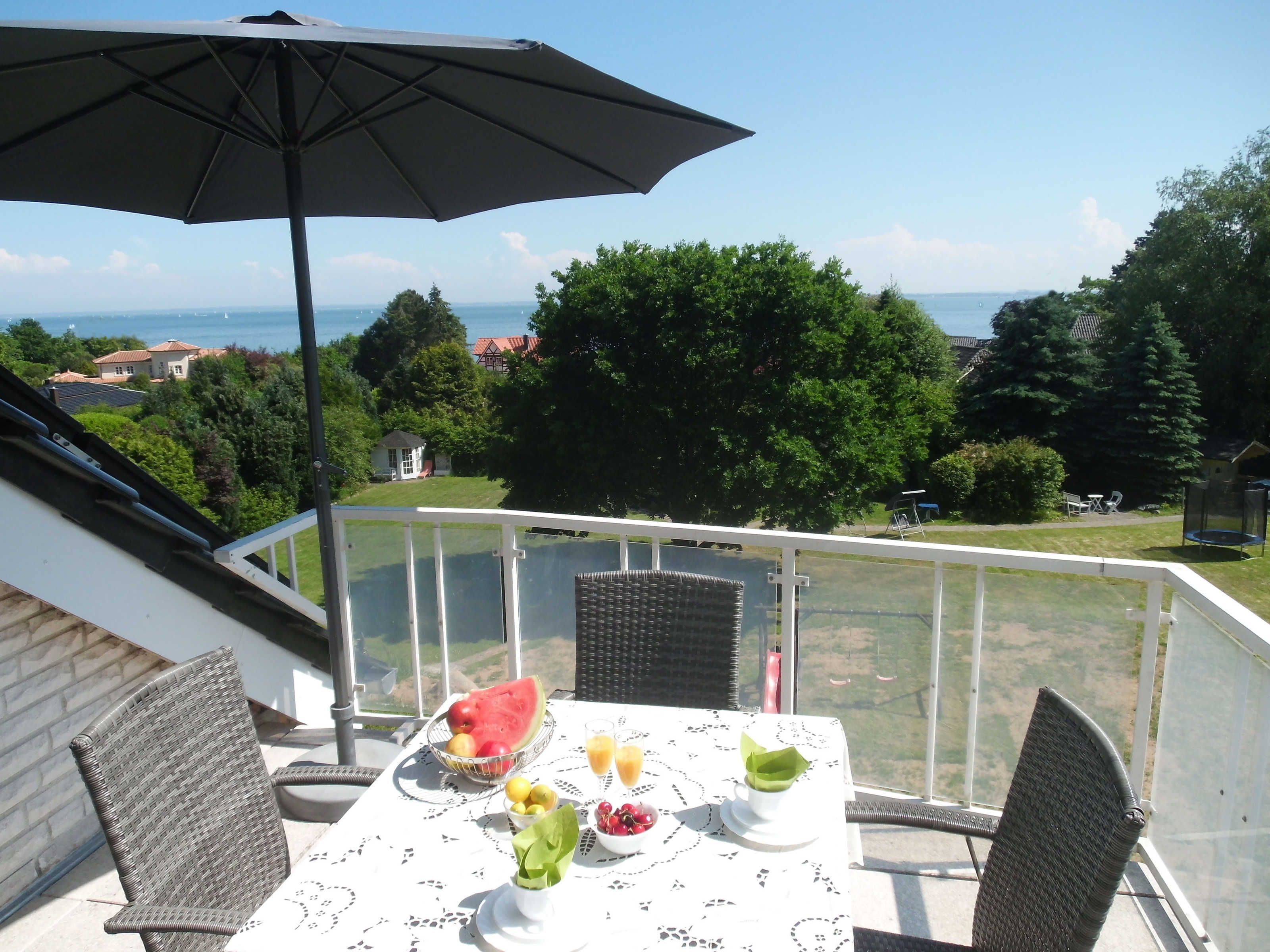 A balcony with a table set for breakfast, a wicker chair, and an umbrella.