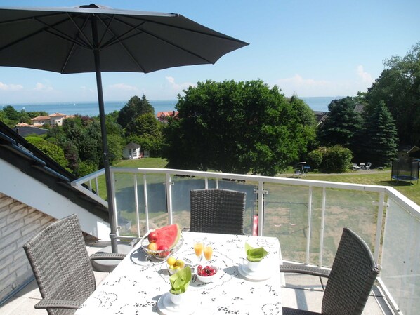 A balcony with a table set for breakfast, a wicker chair, and an umbrella.