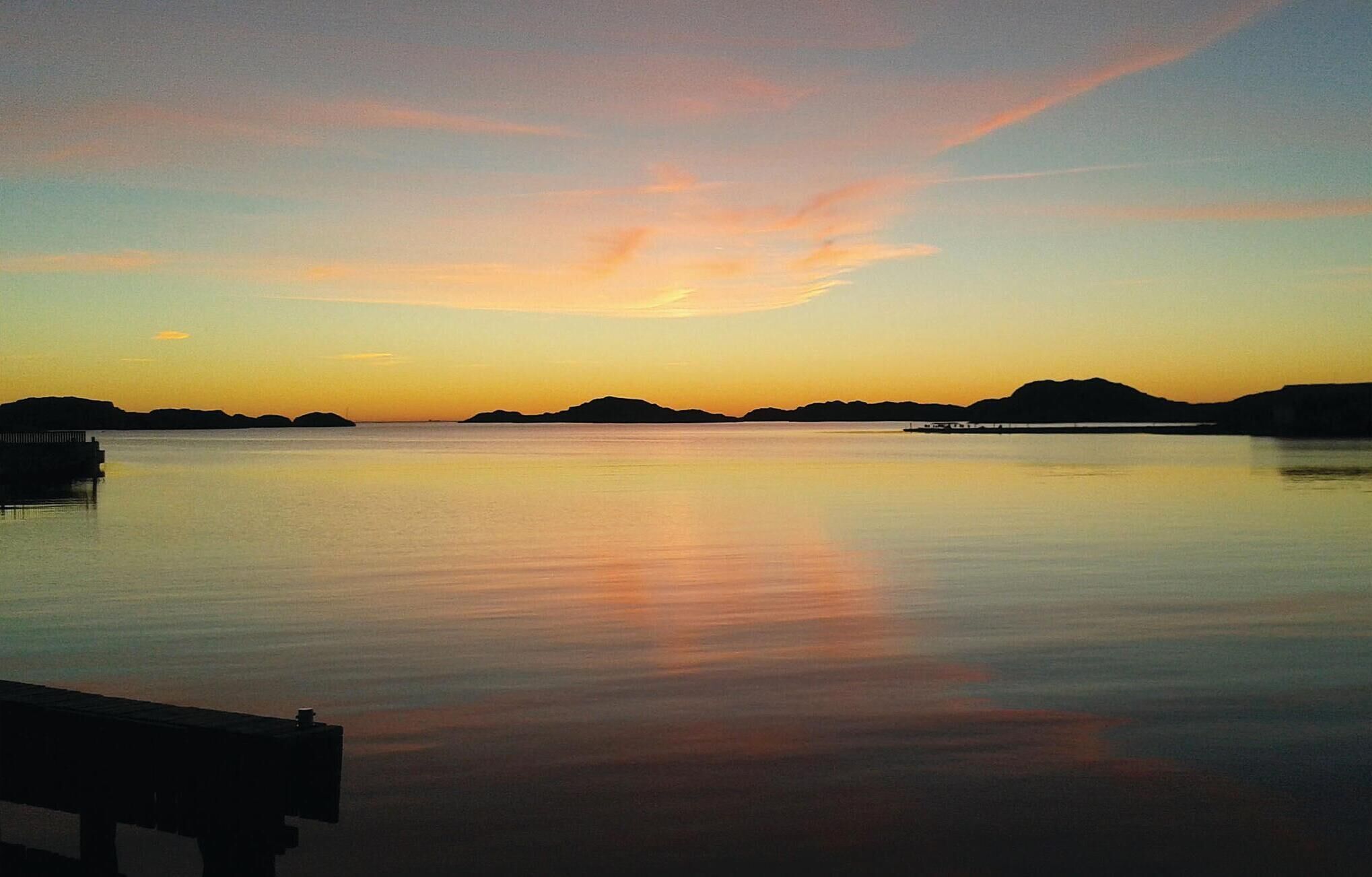 Un plan d'eau calme, avec un quai et des reliefs lointains, au coucher du soleil.